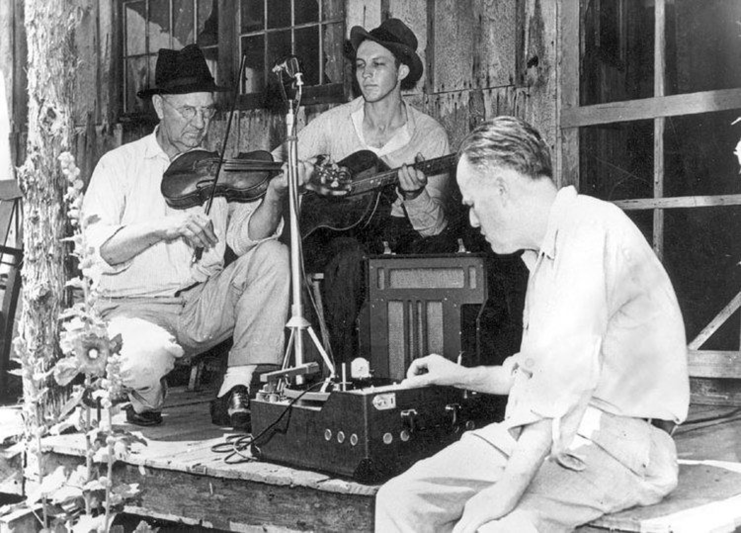 Vance Randolph recording a fiddler and a guitar player on a weathered Ozark porch